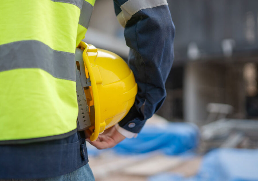 Person in a high-visibility vest holds a hard hat