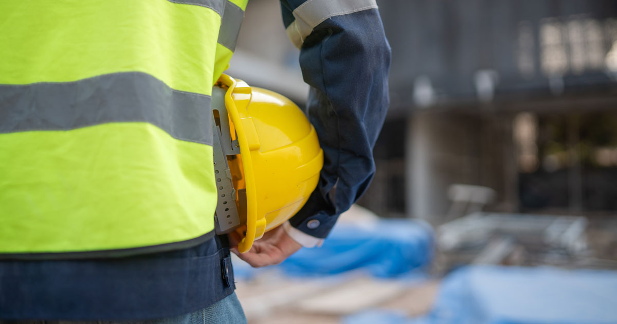 Person in a high-visibility vest holds a hard hat